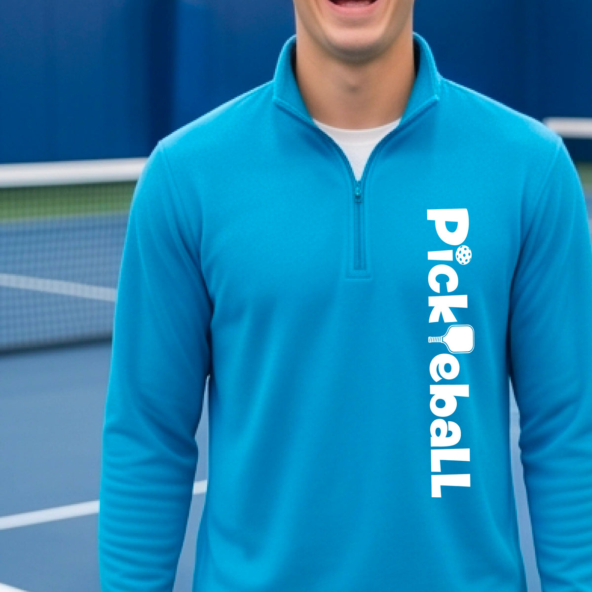 A man wearing a bright blue quarter-zip pullover with 'Pickleball' printed vertically in white on the right side, standing on a blue pickleball court.