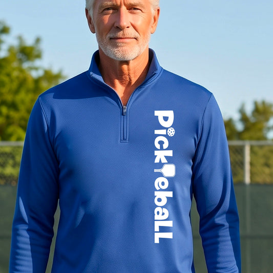 A man wearing a royal blue quarter-zip shirt with a white graphic text 'PICKLEBALL' with a pickleball paddle replacing the L, on the front, standing on a pickleball court.