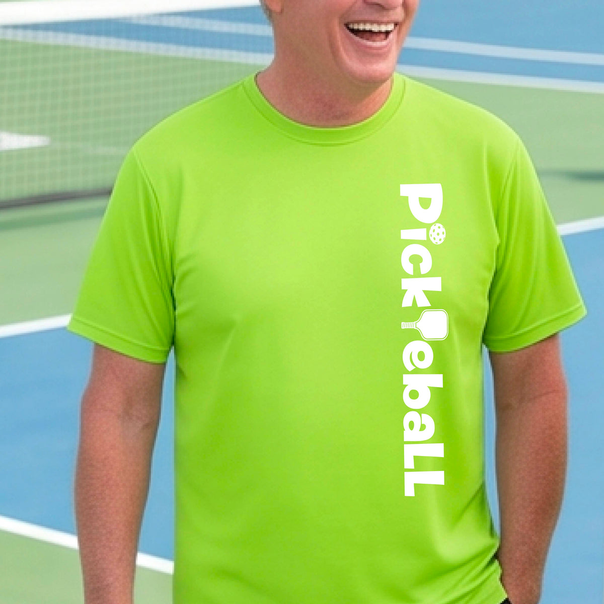 A man wearing a lime green short-sleeve t-shirt with a white graphic text 'PICKLEBALL' with a pickleball paddle replacing the L, on the front, standing on a pickleball court.