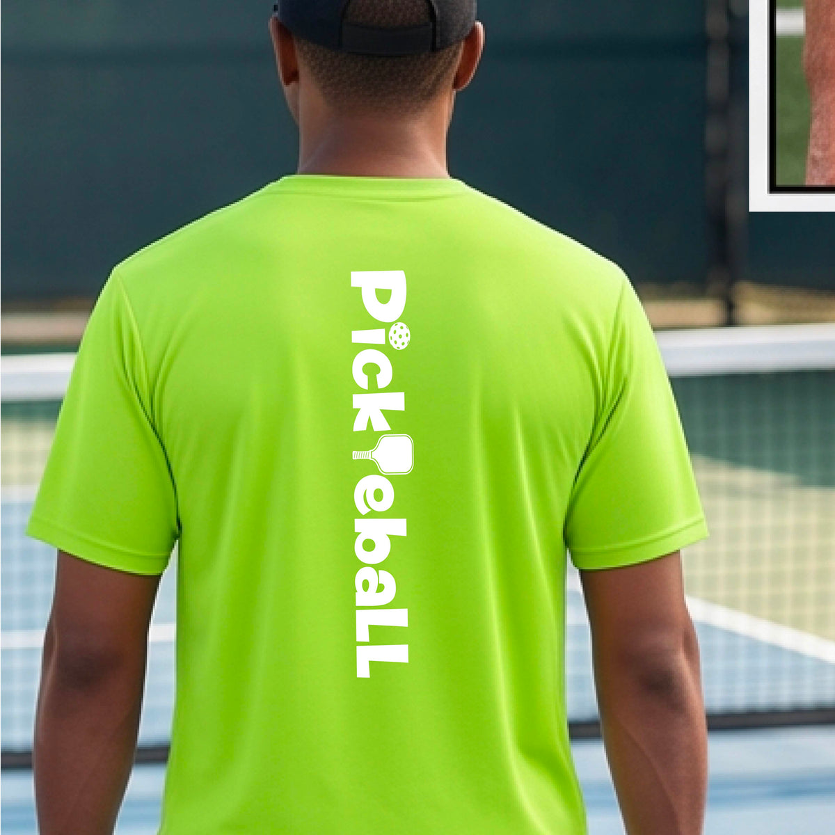 A man wearing a lime green short-sleeve t-shirt with a white graphic text 'PICKLEBALL' with a pickleball paddle replacing the L, on the back, standing on a pickleball court.