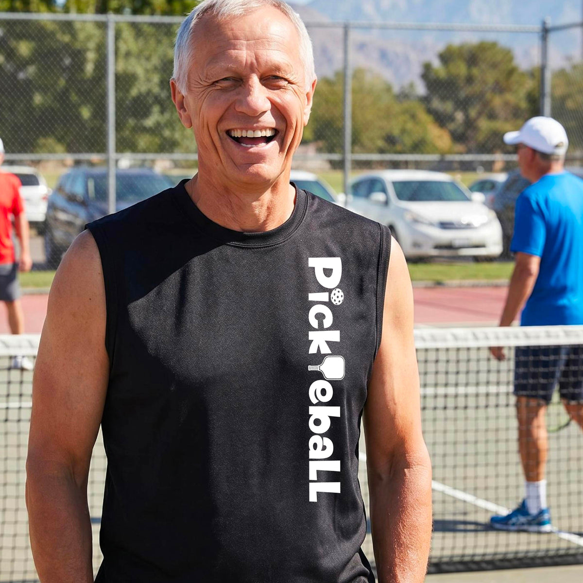 A man wearing a black sleeveless t-shirt with a white graphic text 'PICKLEBALL' with a pickleball paddle replacing the L, on the front, standing on a pickleball court.