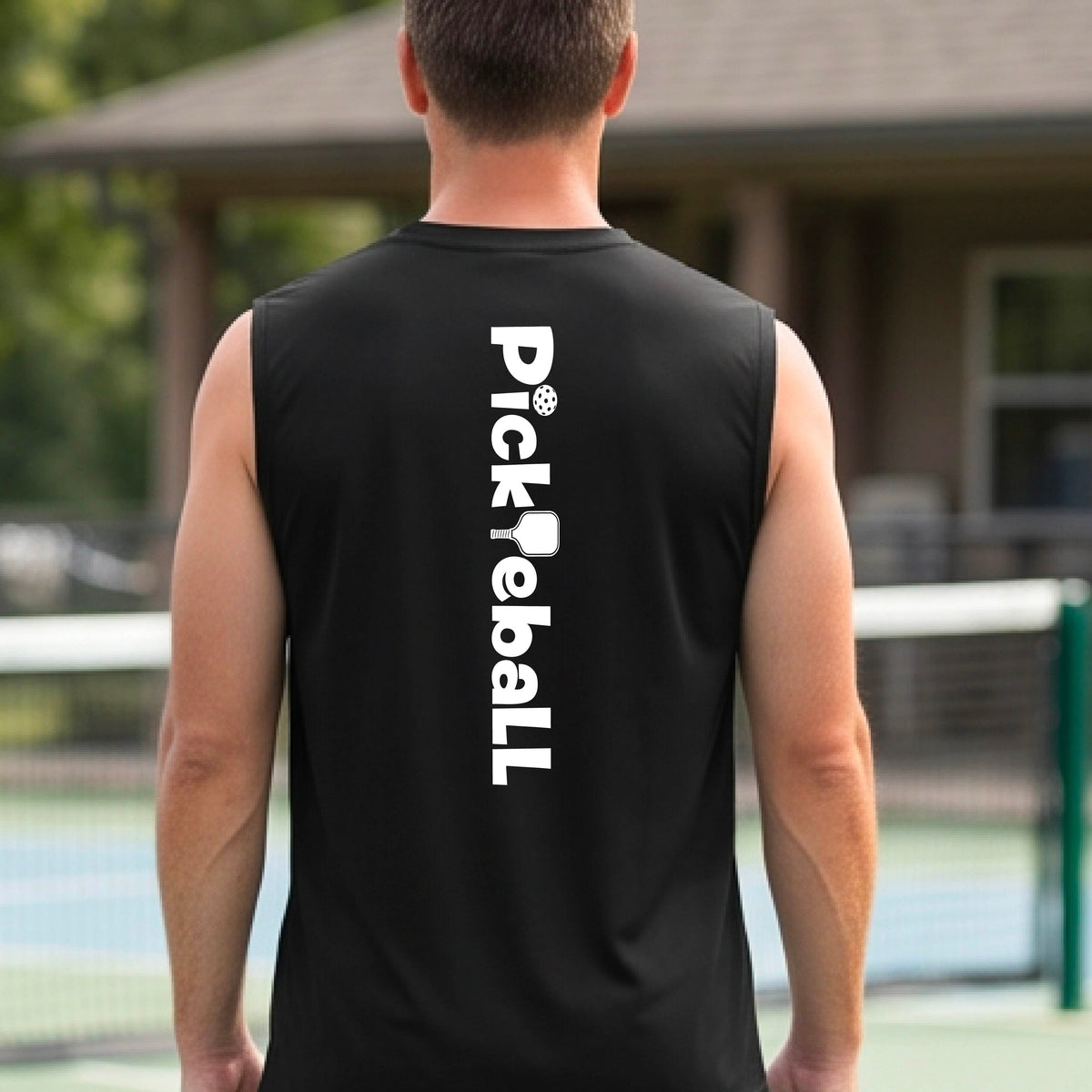 A man wearing a black sleeveless t-shirt with a white graphic text 'PICKLEBALL' with a pickleball paddle replacing the L, on the back, standing on a pickleball court.