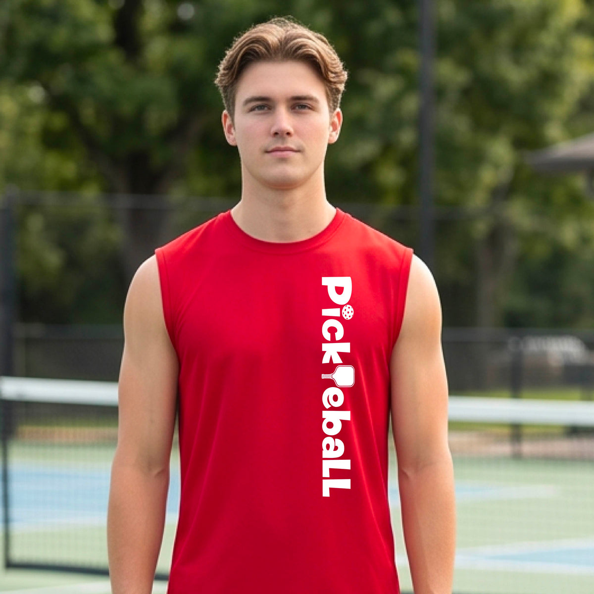 A man wearing a red sleeveless t-shirt with a white graphic text 'PICKLEBALL' with a pickleball paddle replacing the L, on the front, standing on a pickleball court.