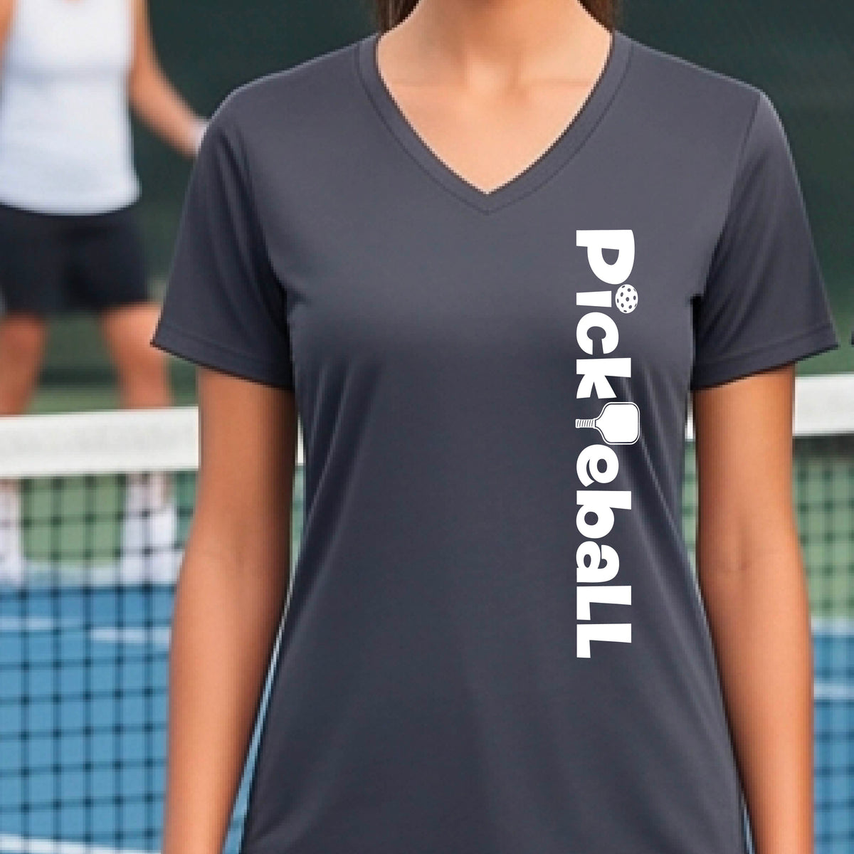 A person wearing a gray short-sleeve athletic T-shirt with a vertical white 'Pickbeall' logo printed on the front right, photographed on a pickleball court.