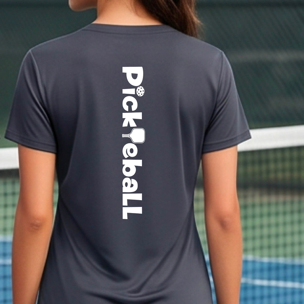 A person wearing a gray short-sleeve athletic T-shirt with a vertical white 'Pickbeall' logo printed on the middle back, photographed on a pickleball court.