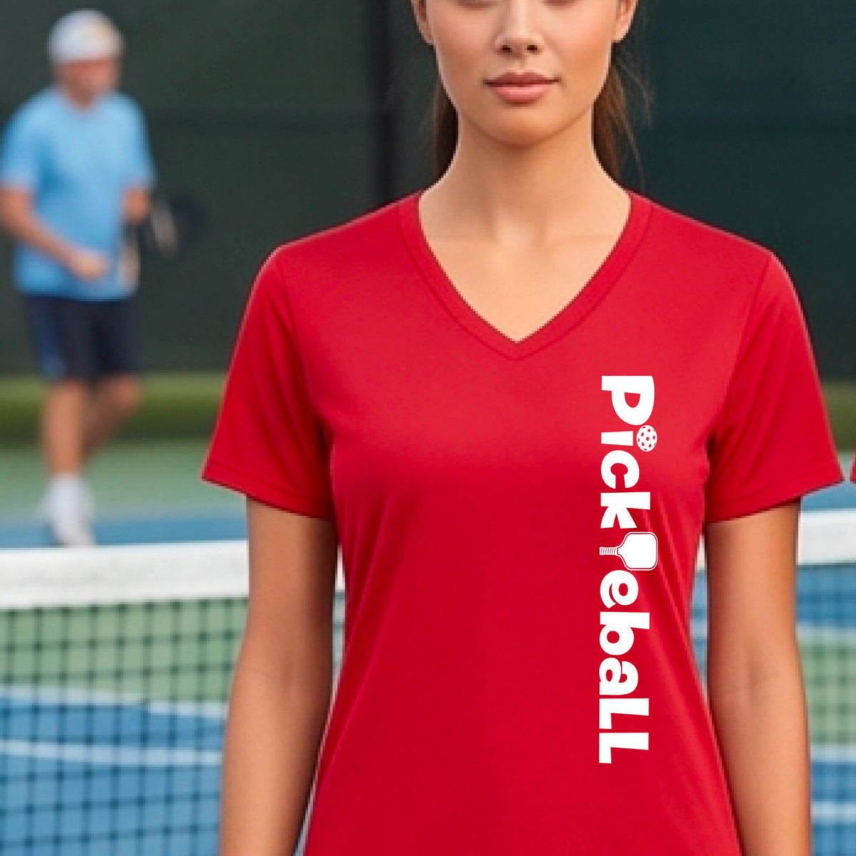 A person wearing a red short-sleeve athletic T-shirt with a vertical white 'Pickbeall' logo printed on the front right, photographed on a pickleball court.