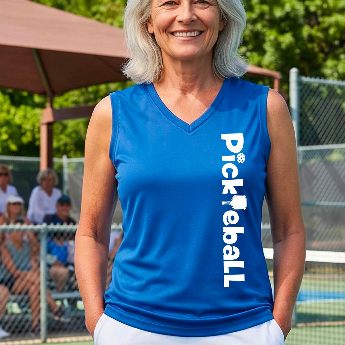 A smiling woman on a pickleball court wearing a bright royal blue sleeveless V-neck athletic top with 'Pickleball' printed vertically in white on the front.