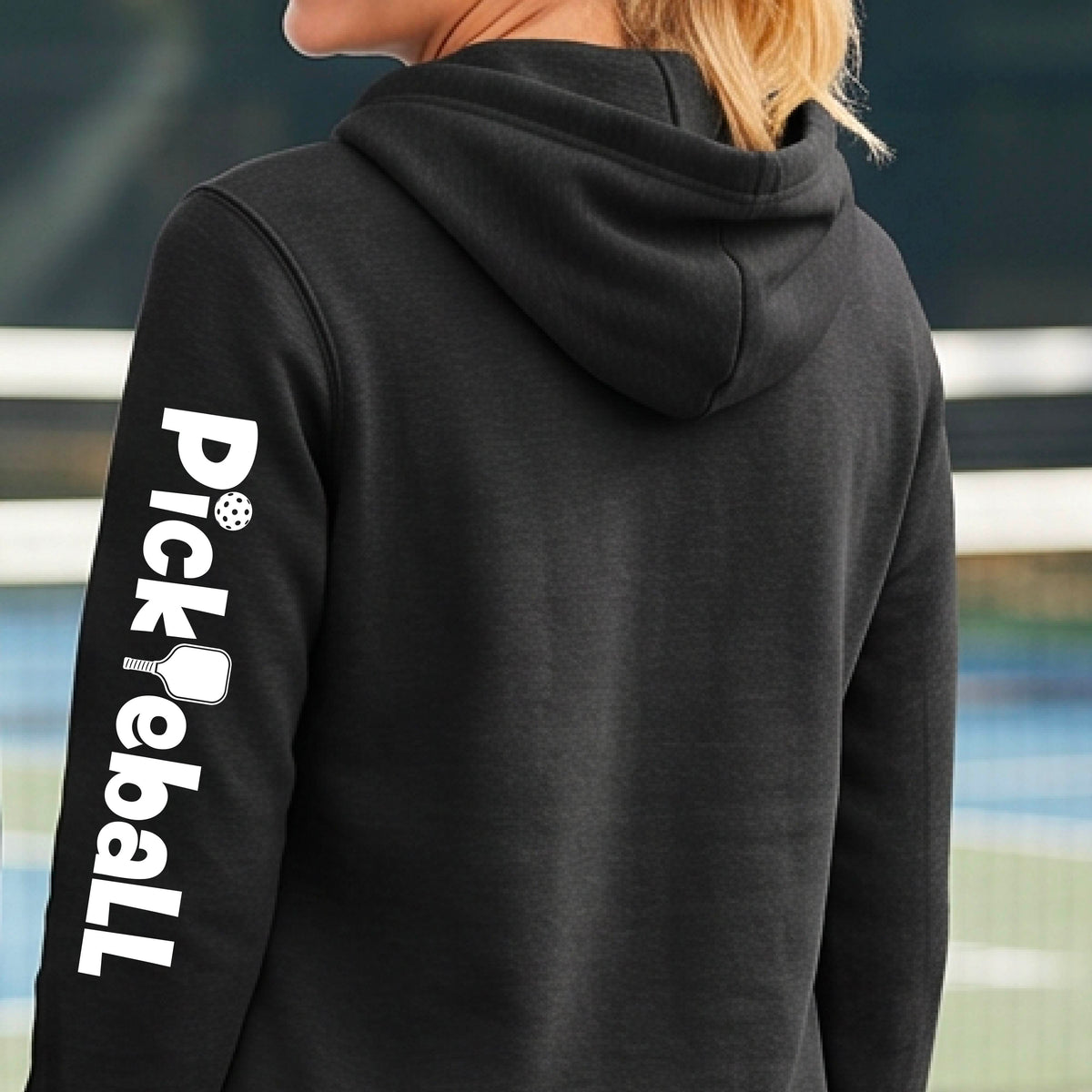 A person wearing a dark charcoal gray hoodie, shown from the back and side. The left sleeve features a large white vertical graphic that reads 'Pickleball' with a pickleball icon.