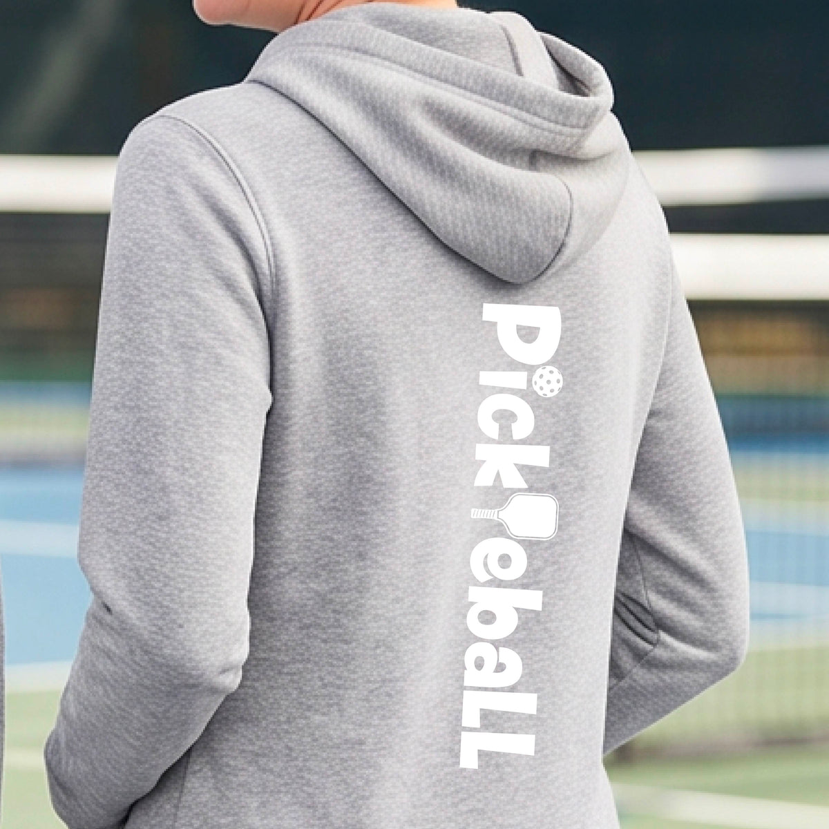 A person wearing a heather gray hoodie, shown from the back. The hoodie features the word 'Pickleball' printed vertically in white on the back, with a pickleball icon integrated into the lettering.