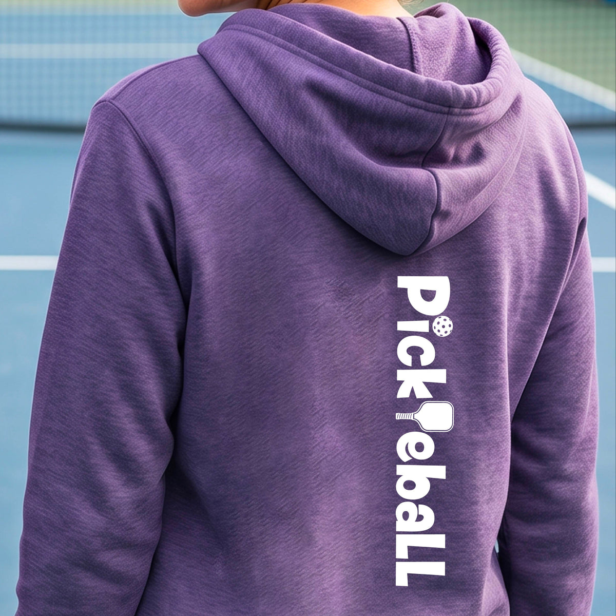 A person viewed from behind wearing a heather purple hoodie with a vertical white 'Pickball' graphic printed on the back, standing on a blue tennis court.