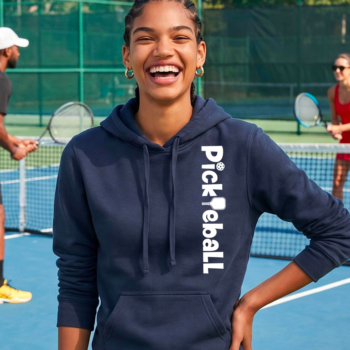 A woman smiling on a pickelball court wearing a navy blue hoodie with 'Pickleball' printed vertically in white on the chest.