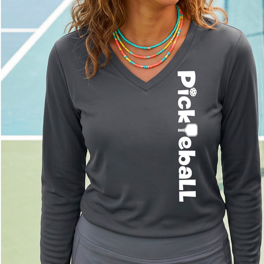 A woman wearing a gray long-sleeve t-shirt with a white graphic text 'PICKLEBALL' with a pickleball paddle replacing the L, on the front, standing on a pickleball court.
