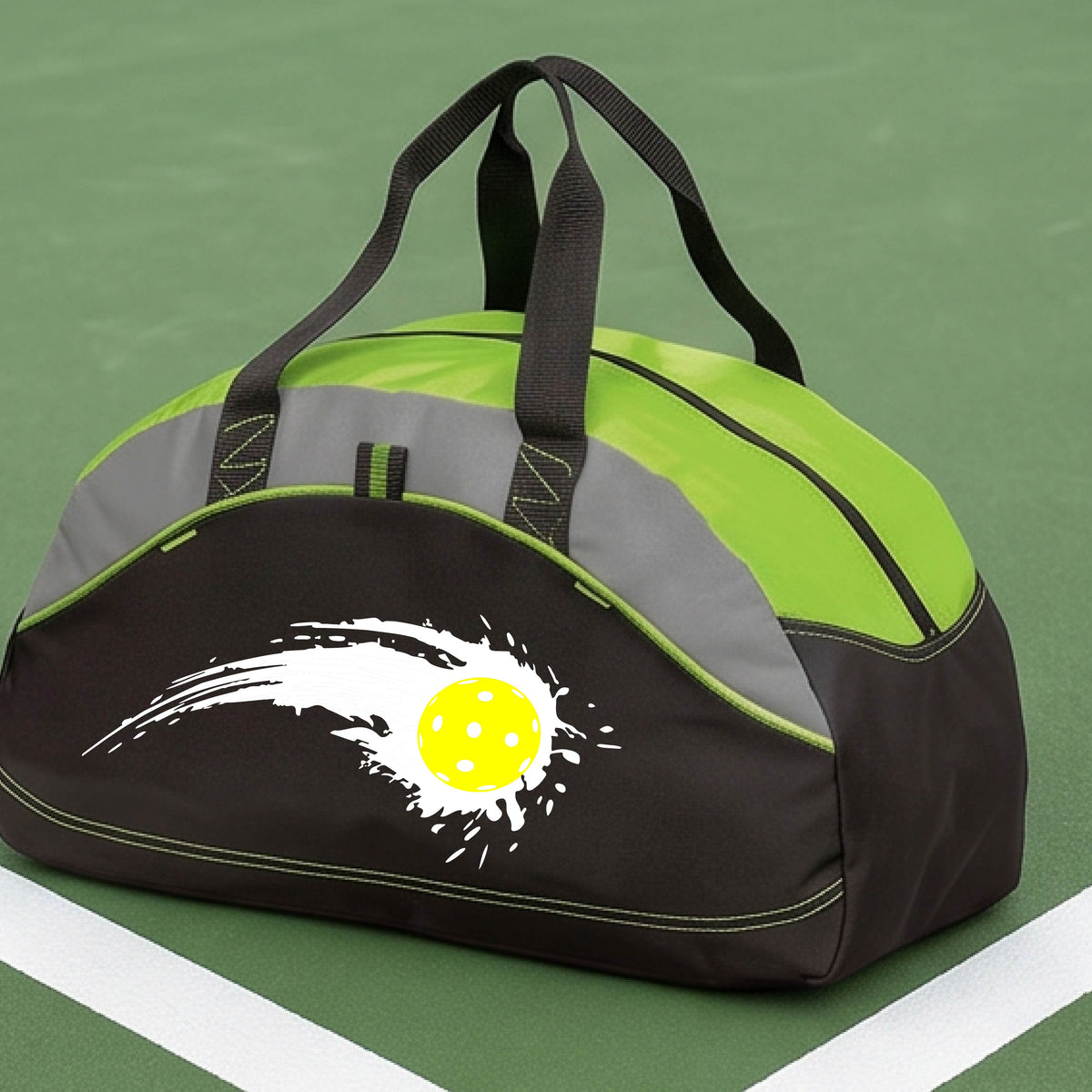 A close-up of a lime green, black and gray medium size duffel bag with a white pickleball graphic of a yellow pickleball with a motion trail effect, displayed in front of a pickleball court. 