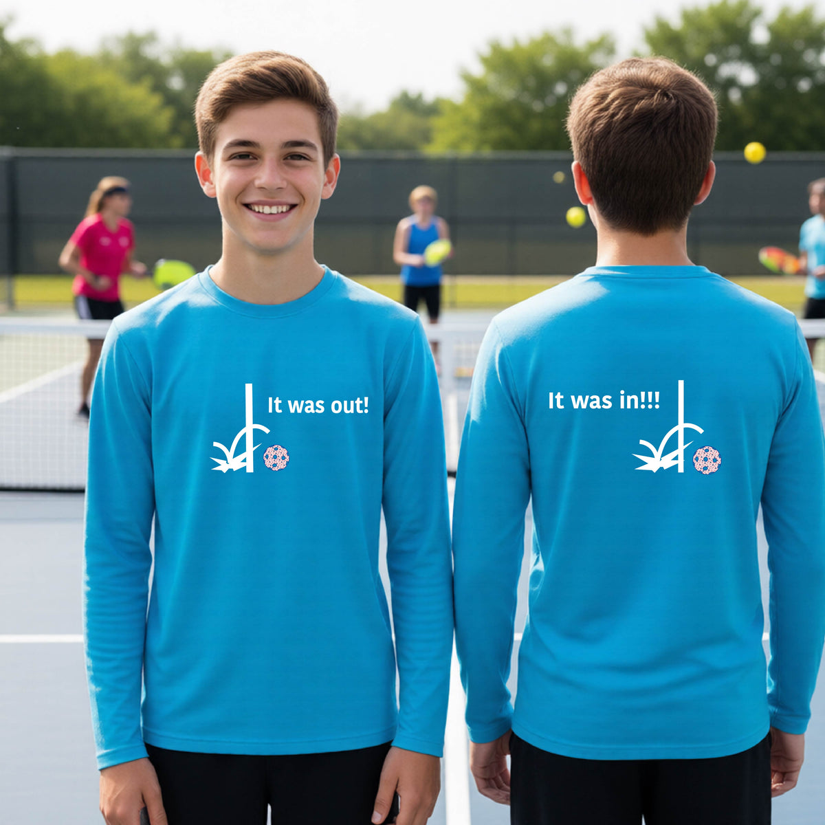 Two youths showing a bright blue  long-sleeve t-shirt with a white design of ‘IT WAS OUT!’ and a colorful pickleball on the front, and the back design with a white ‘IT WAS IN!!!’ and a colorful pickleball, standing on a pickleball court.