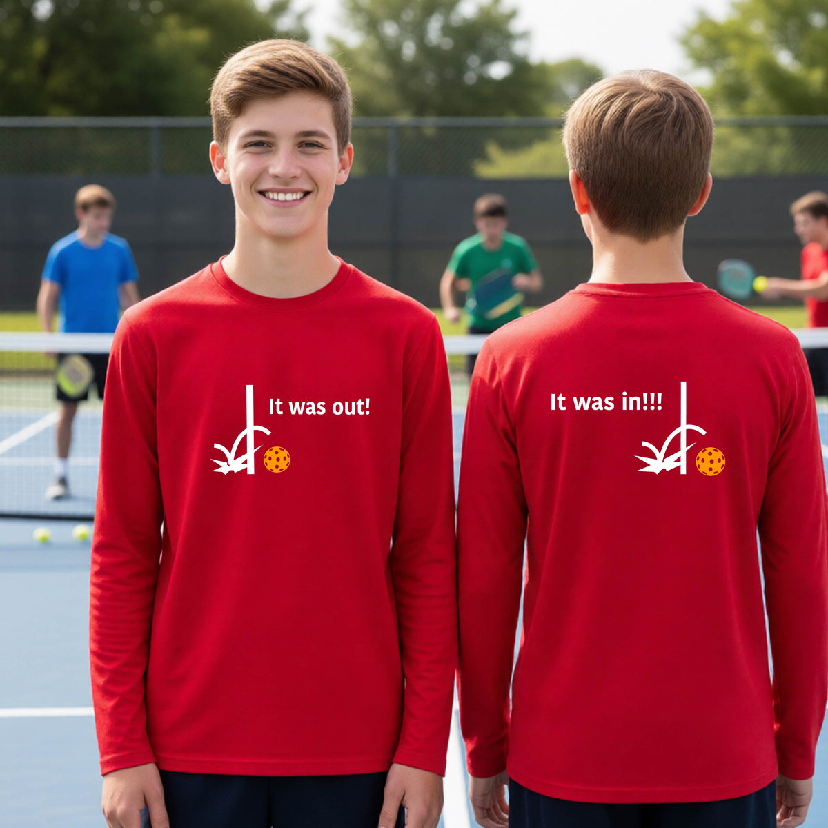 Two youths showing a red long-sleeve t-shirt with a white design of ‘IT WAS OUT!’ and a colorful pickleball on the front, and the back design with a white ‘IT WAS IN!!!’ and a colorful pickleball, standing on a pickleball court.