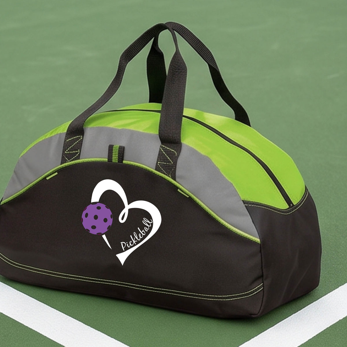 A black and lime green pickleball duffel bag with a white heart logo and purple pickleball graphic, resting on a green pickleball court.