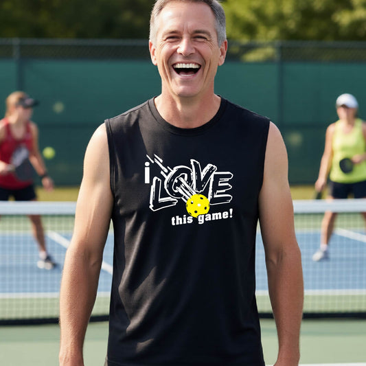 A smiling man on a pickleball court wearing a blacksleeveless tank top with a white graphic that reads 'i LOVE this game!' and a yellow pickleball detail.