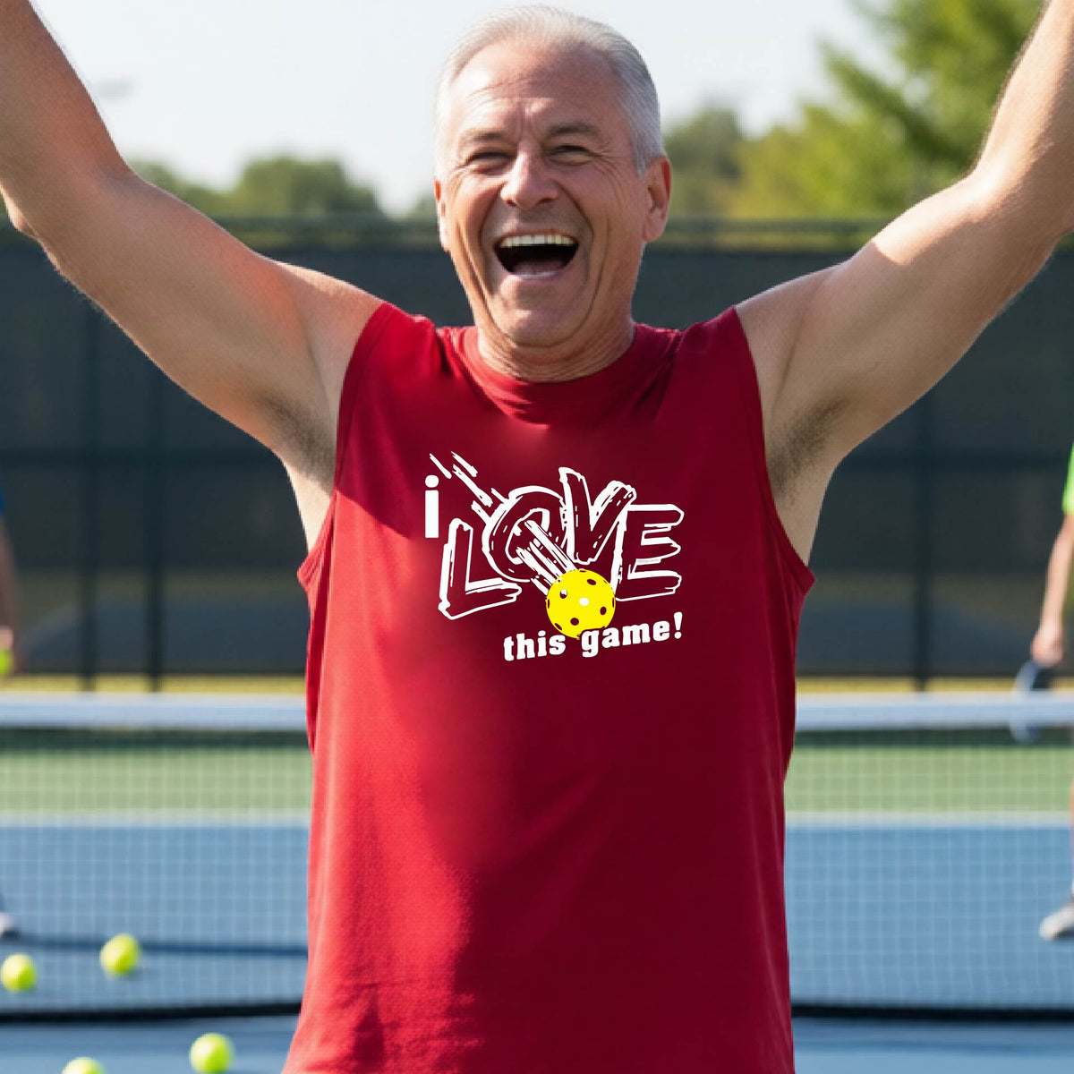 A smiling man on a pickleball court wearing a red sleeveless tank top with a white graphic that reads 'i LOVE this game!' and a yellow pickleball detail.