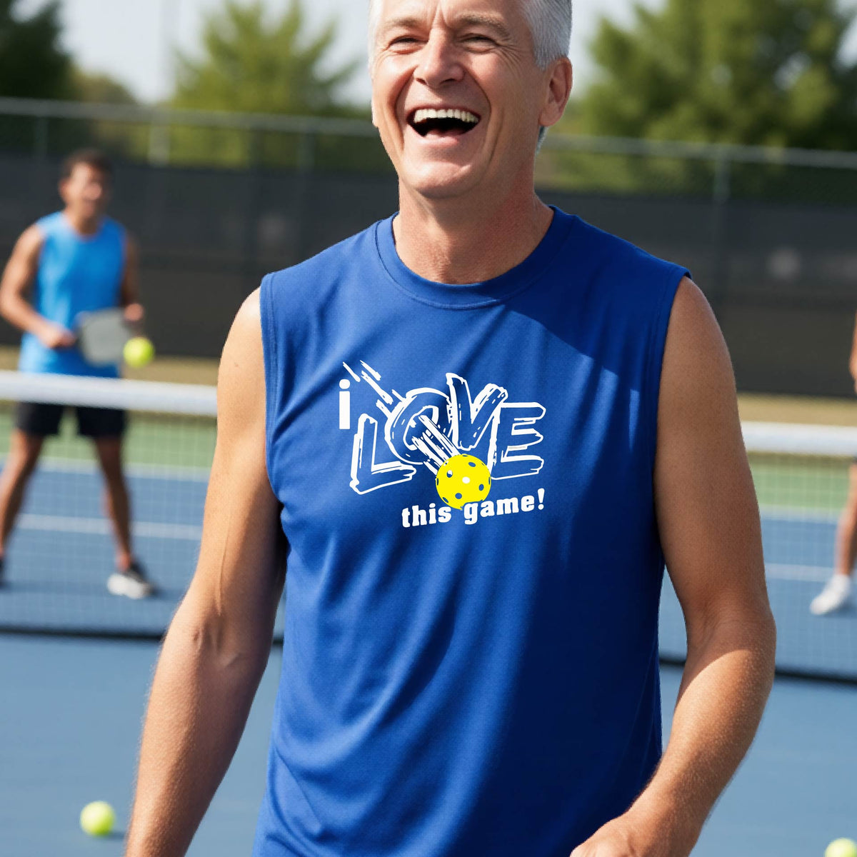 A smiling man on a pickleball court wearing a royal blue sleeveless tank top with a white graphic that reads 'i LOVE this game!' and a yellow pickleball detail.