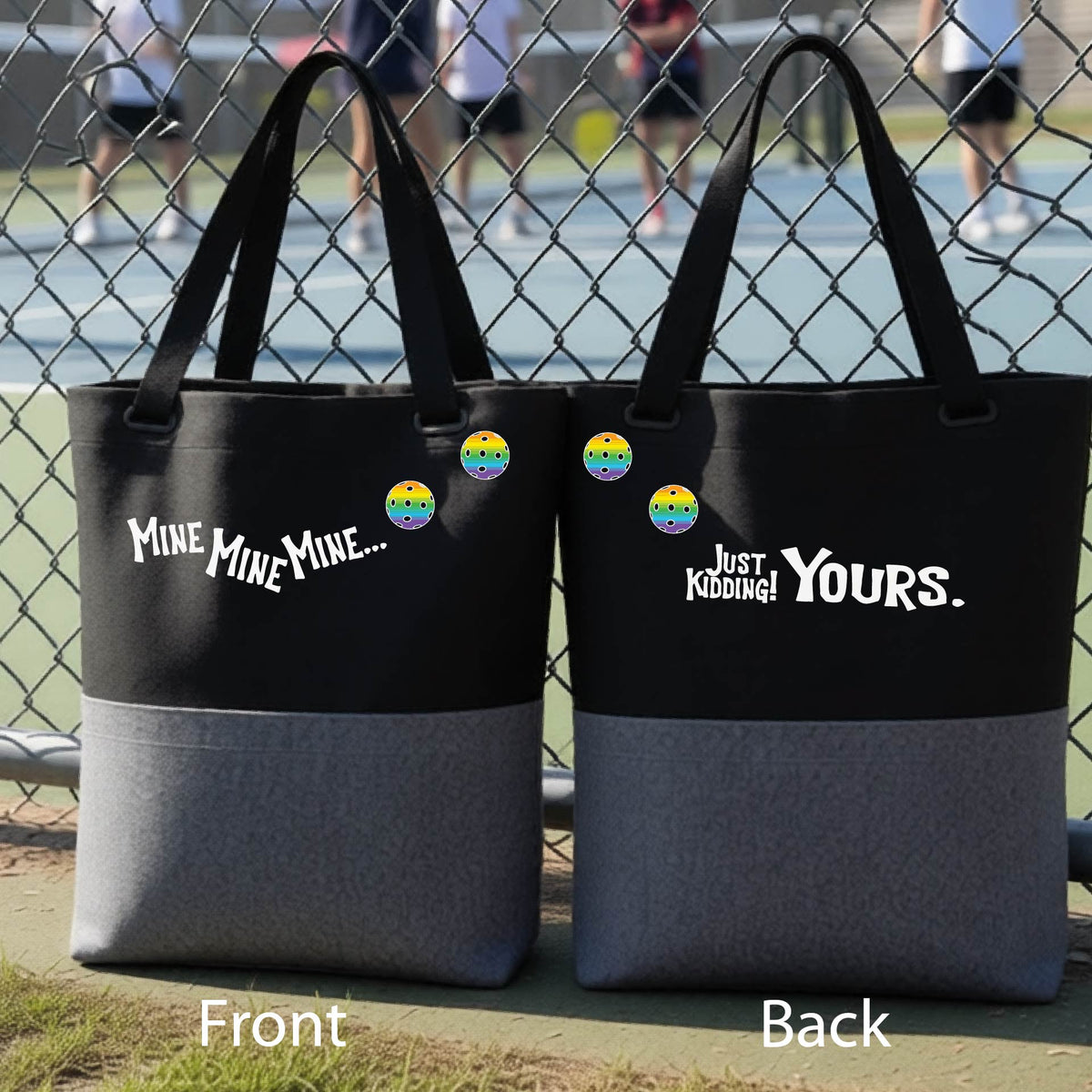 A close-up of two black and gray tote bags.  One shows the front with the text 'MINE MINE MINE' along with three pickleball graphics. and the back text 'JUST KIDDING YOURS, along with three pickleball graphics, in front of a pickleball court. 