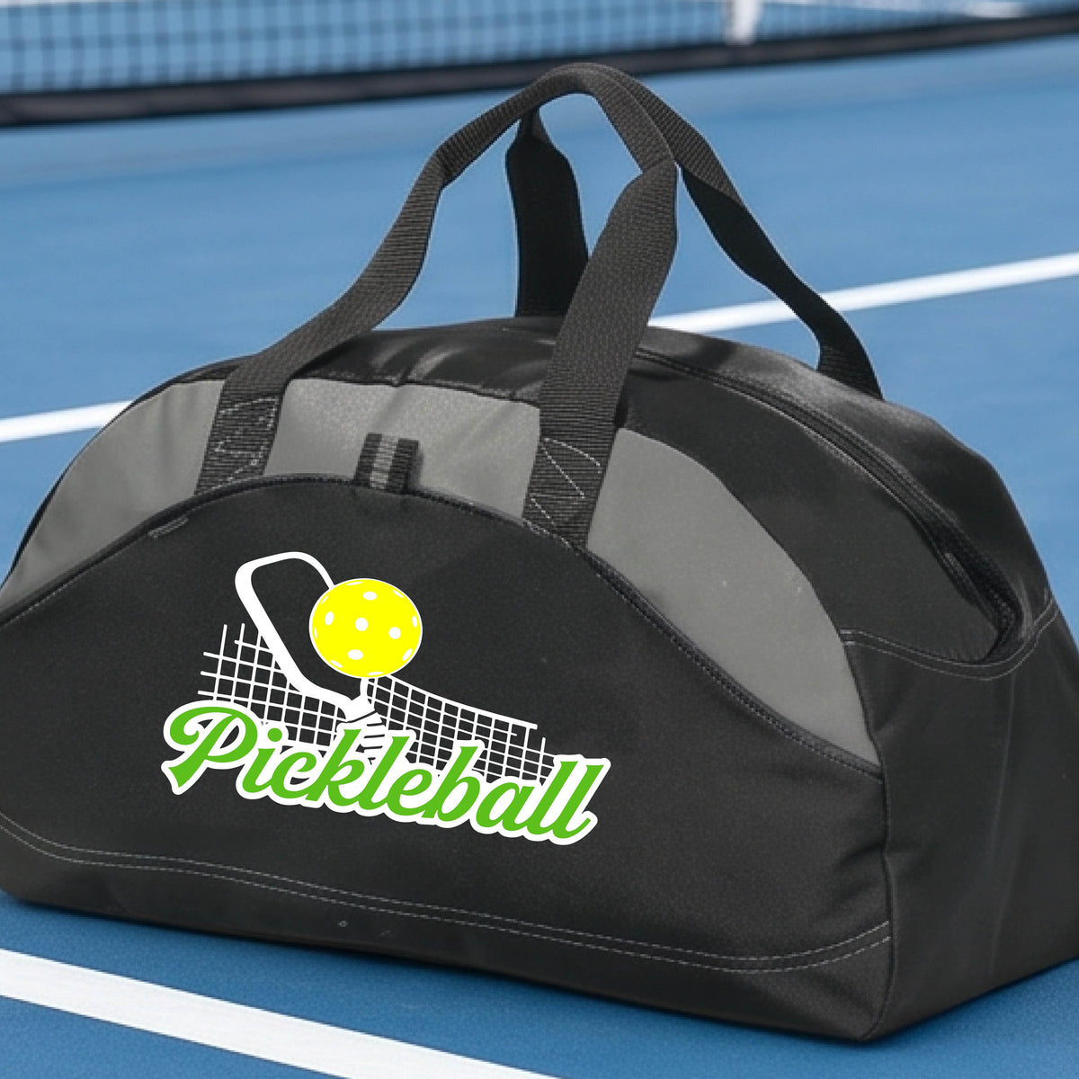 A close-up of a black and gray tote bag with a graphic on the front that has white and green text "PICKLEBALL'  with a white pickleball paddle and net and a yellow pickleball above the text graphic.