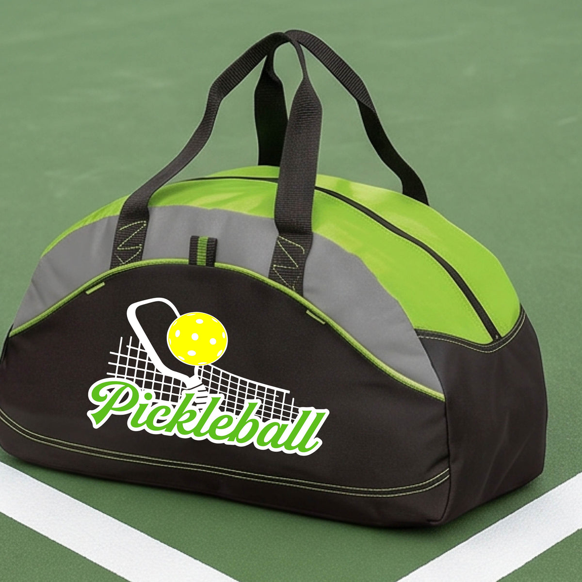 A close-up of a green, black and gray tote bag with a graphic on the front that has white and green text "PICKLEBALL'  with a white pickleball paddle and net and a yellow pickleball above the text graphic.