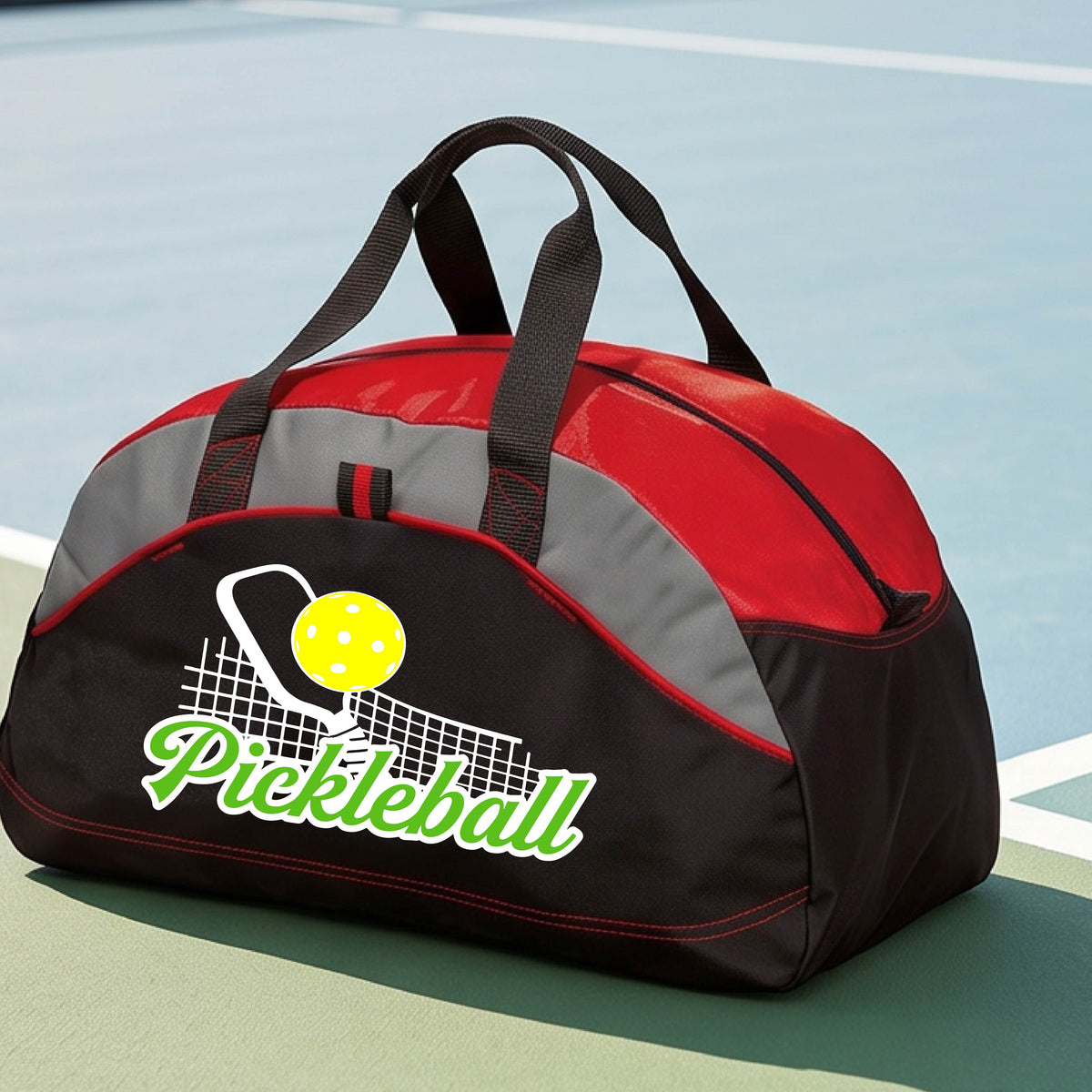 A close-up of a red, black and gray tote bag with a graphic on the front that has white and green text "PICKLEBALL'  with a white pickleball paddle and net and a yellow pickleball above the text graphic.