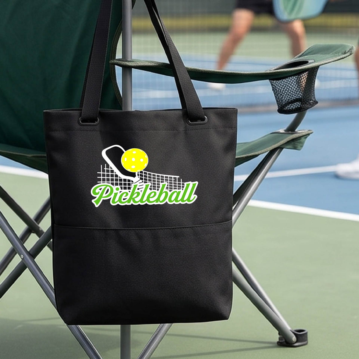 A close-up of a black tote bag with a graphic on the front that has white and green text "PICKLEBALL'  with a white pickleball paddle and net and a yellow pickleball above the text graphic.
