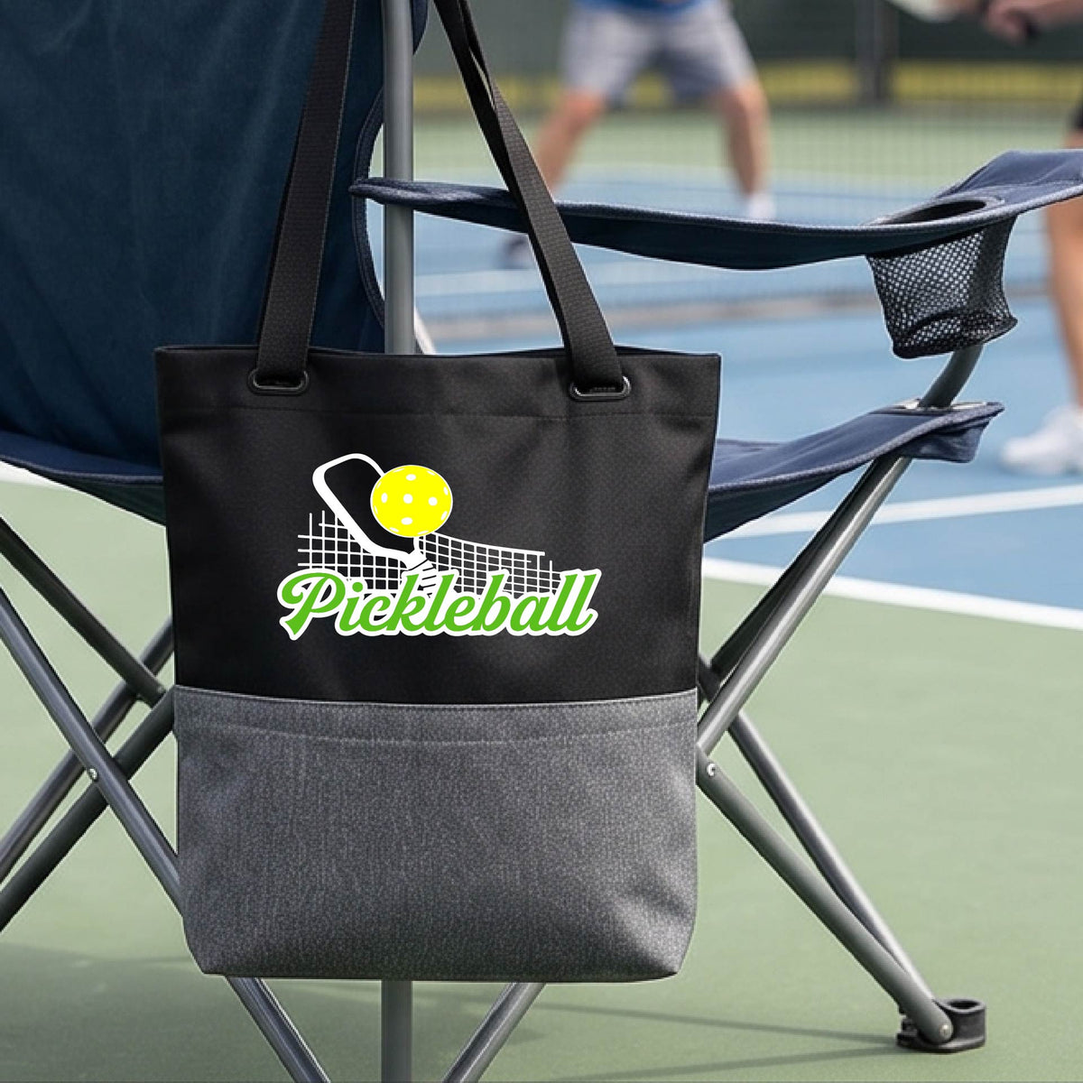 A close-up of a black and gray tote bag with a graphic on the front that has white and green text "PICKLEBALL'  with a white pickleball paddle and net and a yellow pickleball above the text graphic.