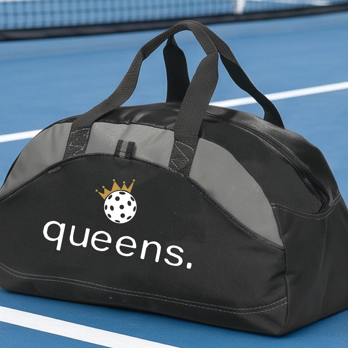 A custom black duffel bag with gray panels, featuring the word 'queens.' and a gold crown, and a white pickleball logo on the front.