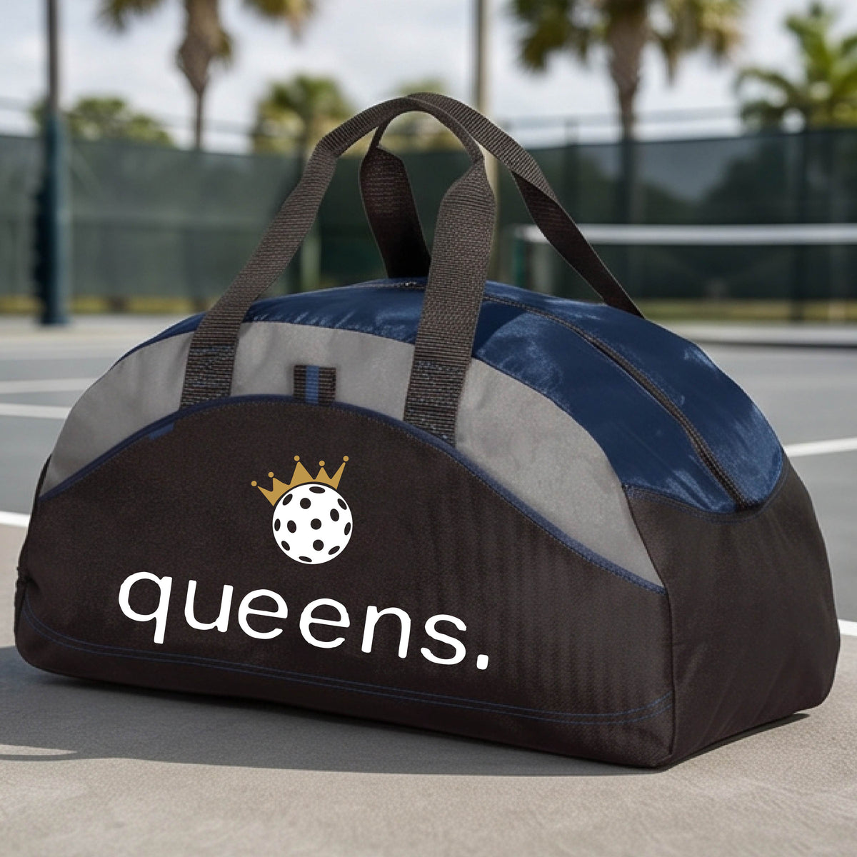 A custom black and navy blue duffel bag with gray panels, featuring the word 'queens.' and a gold crown, and a white pickleball logo on the front.