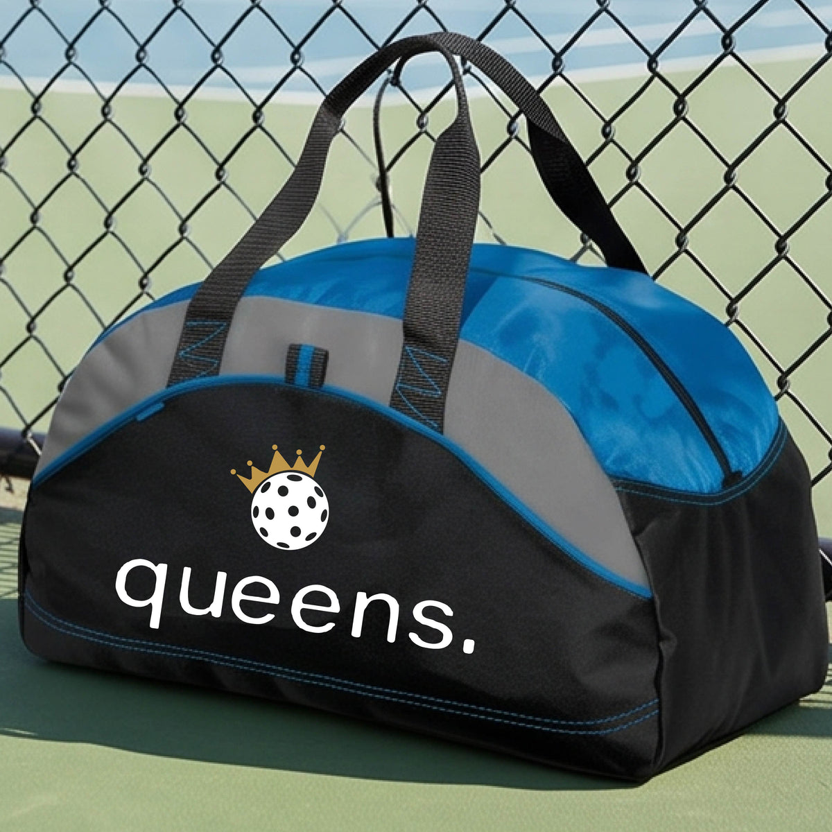 A custom black and royal blue duffel bag with gray panels, featuring the word 'queens.' and a gold crown, and a white pickleball logo on the front.