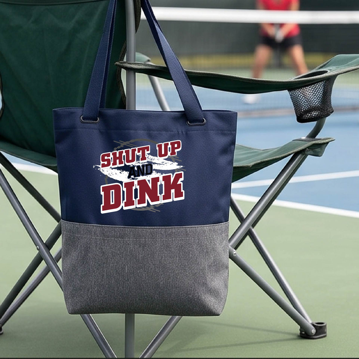 A close up of a navy blue and gray medium size tote bag with a white, gray and black graphic of the text: ‘Shut Up and Dink, on a pickleball court.