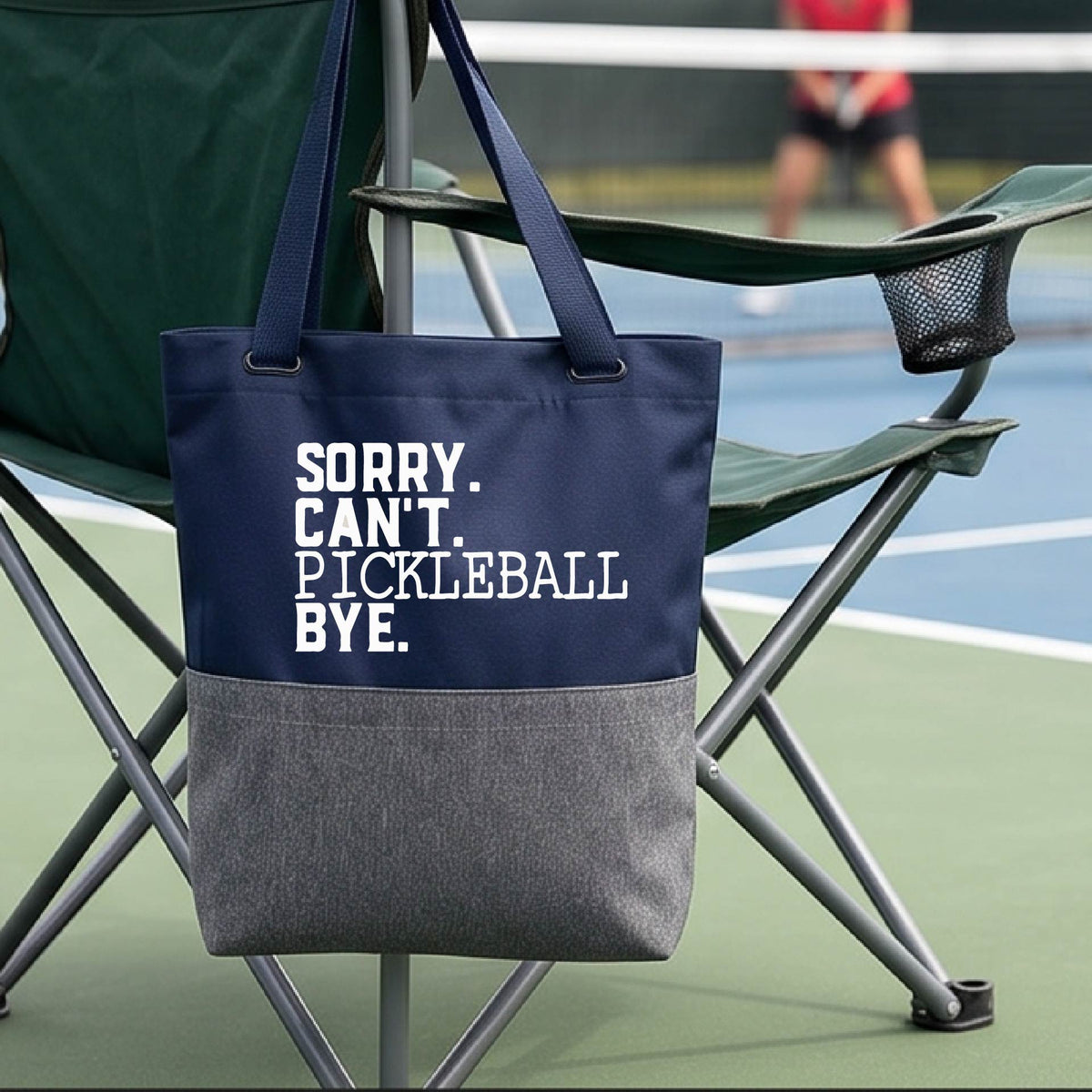 A close up of a grey and blue medium size tote bag on a pickleball court with a white graphic of the words  “SORRY. CAN’T. PICKLEBALL BYE” each on a separate line, on the front. 