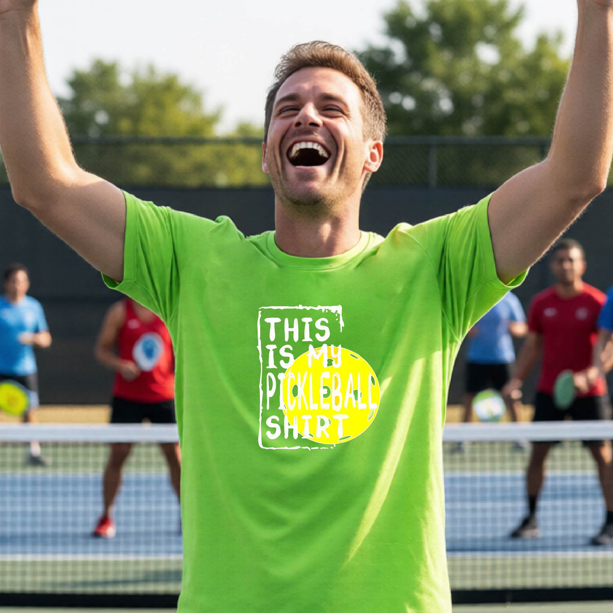 A man on an outdoor pickleball court wearing a lime green t-shirt with a graphic that reads 'THIS IS MY PICKLEBALL SHIRT' in white with a yellow pickleball icon. 