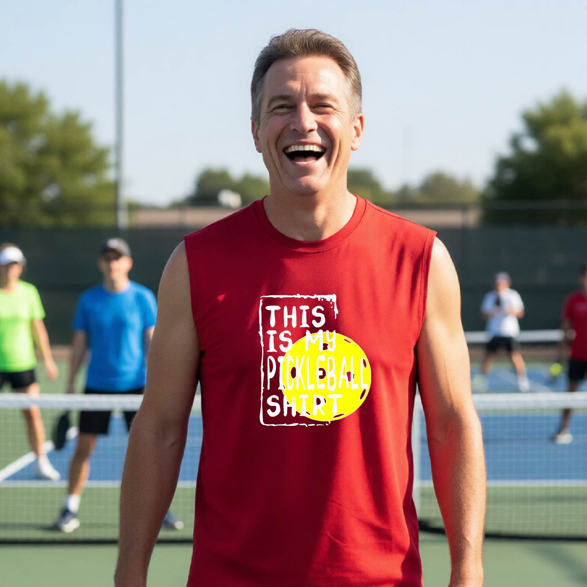 A man on a pickleball court wearing a red sleeveless shirt with a yellow and white graphic that reads 'THIS IS MY PICKLEBALL SHIRT' and a yellow pickleball icon.