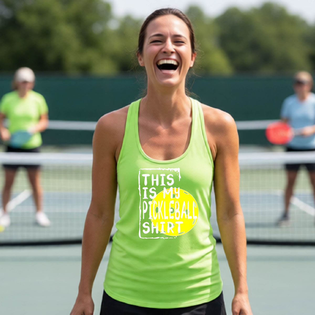 A woman laughing on a pickleball court wearing a lime green tank top with a graphic that reads 'THIS IS MY PICKLEBALL SHIRT' in white with a yellow pickelball graphic.