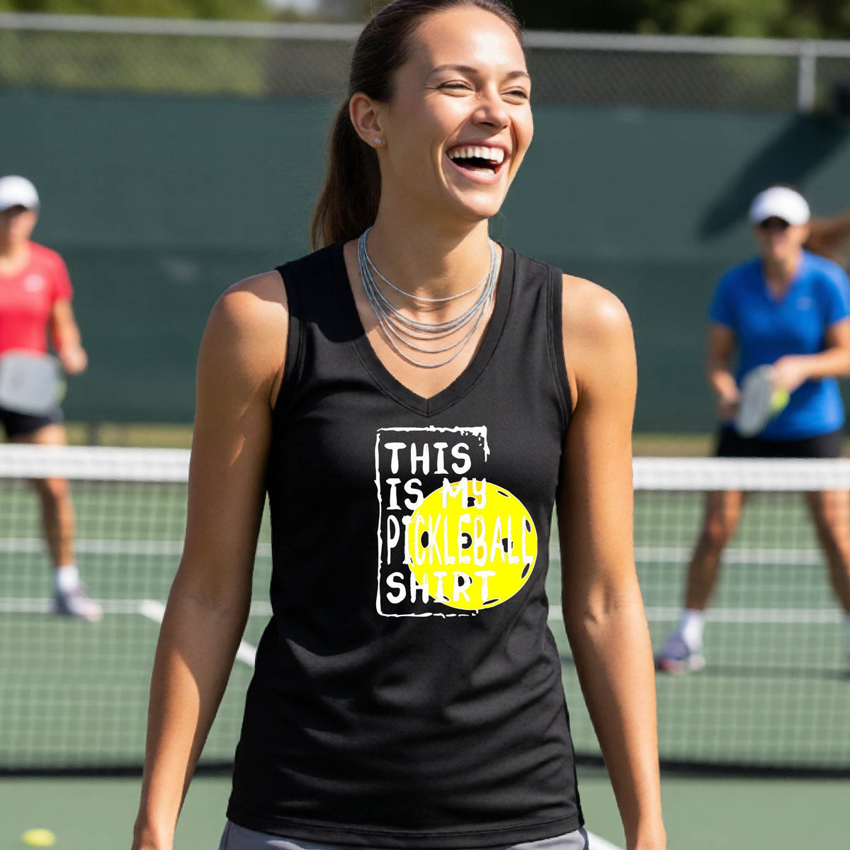 A woman on a pickleball court wearing a black tank top with a yellow and white graphic that reads 'THIS IS MY PICKLEBALL SHIRT' including the yellow pickleball icon.
