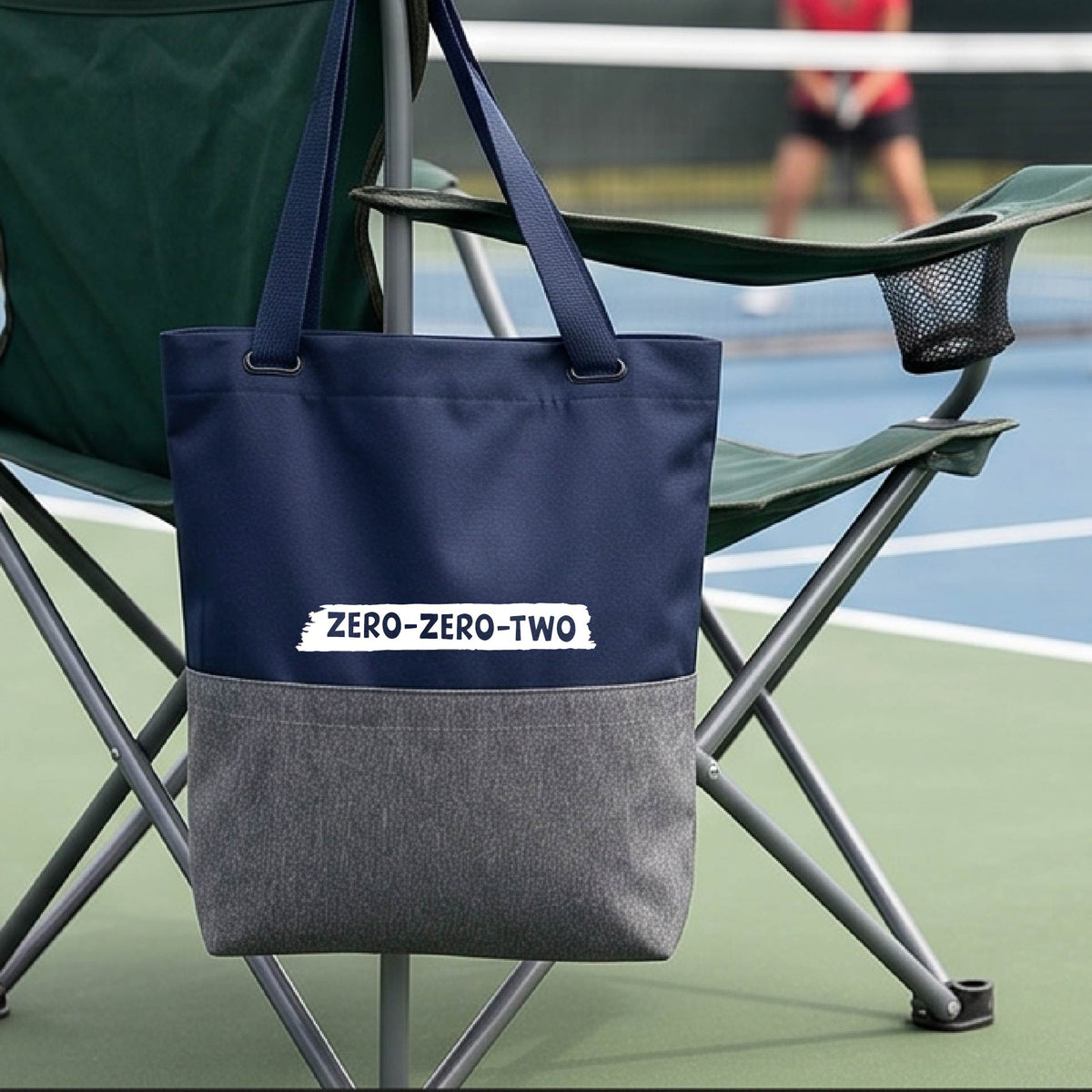 A close-up of a blue and gray medium size tote bak, with a white graphic of artistic banner with the cutout words of ‘ZERO ZERO TWO’, on the bag. 