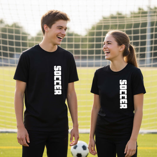 Two young students on a soccer field holding a soccer ball, wearing a black t-shirt with a white graphic of the word 'SOCCER' in block font printed down the side of the shirt