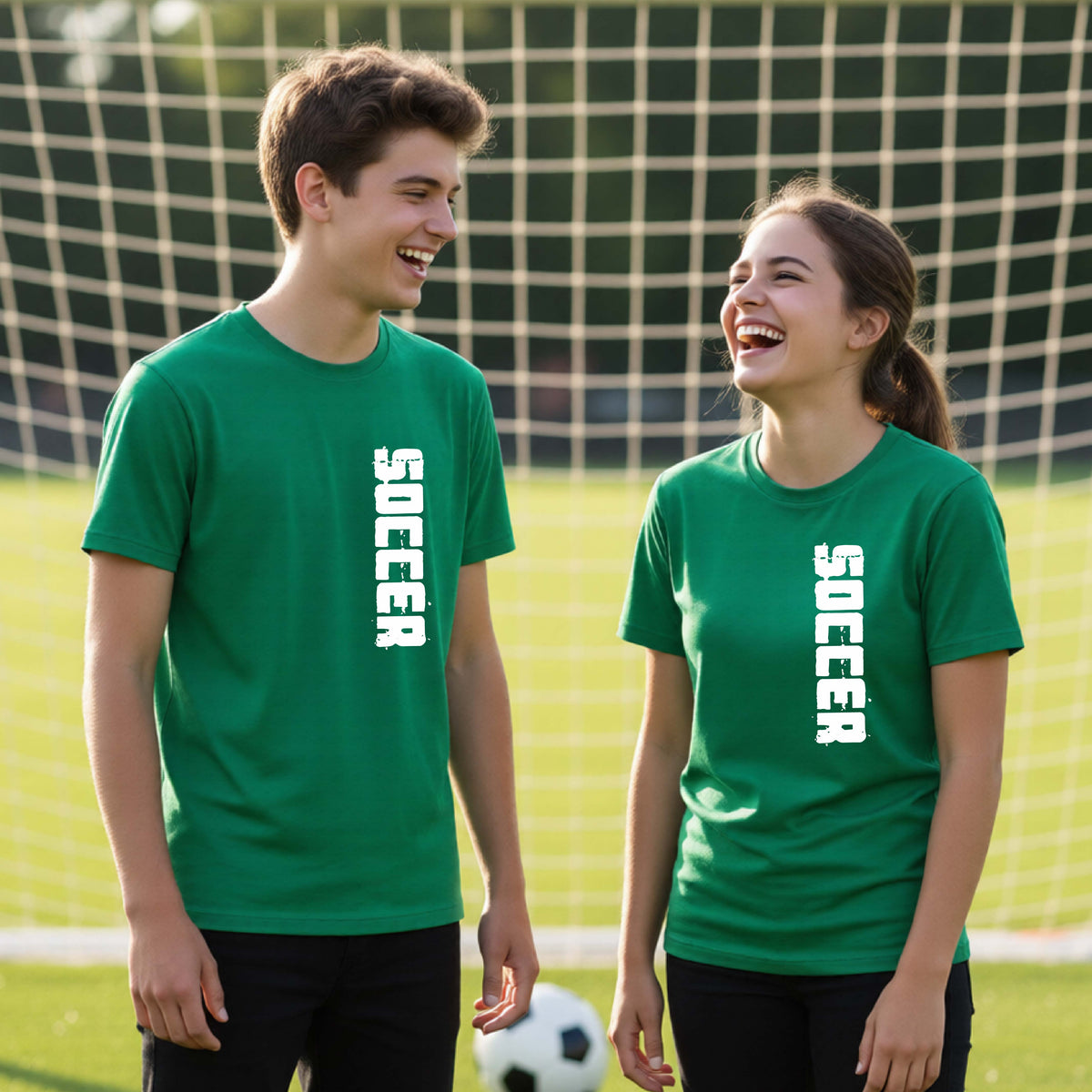 Two young students on a soccer field holding a soccer ball, wearing a green t-shirt with a white graphic of the word 'SOCCER' in block font printed down the side of the shirt