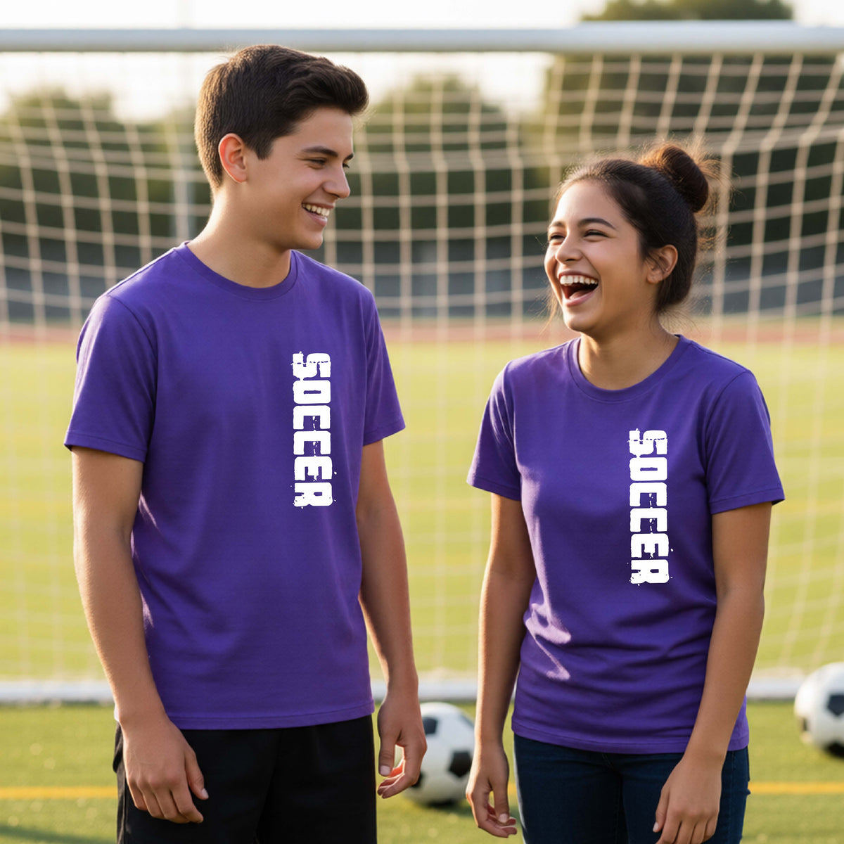 Two young students on a soccer field holding a soccer ball, wearing a purple t-shirt with a white graphic of the word 'SOCCER' in block font printed down the side of the shirt