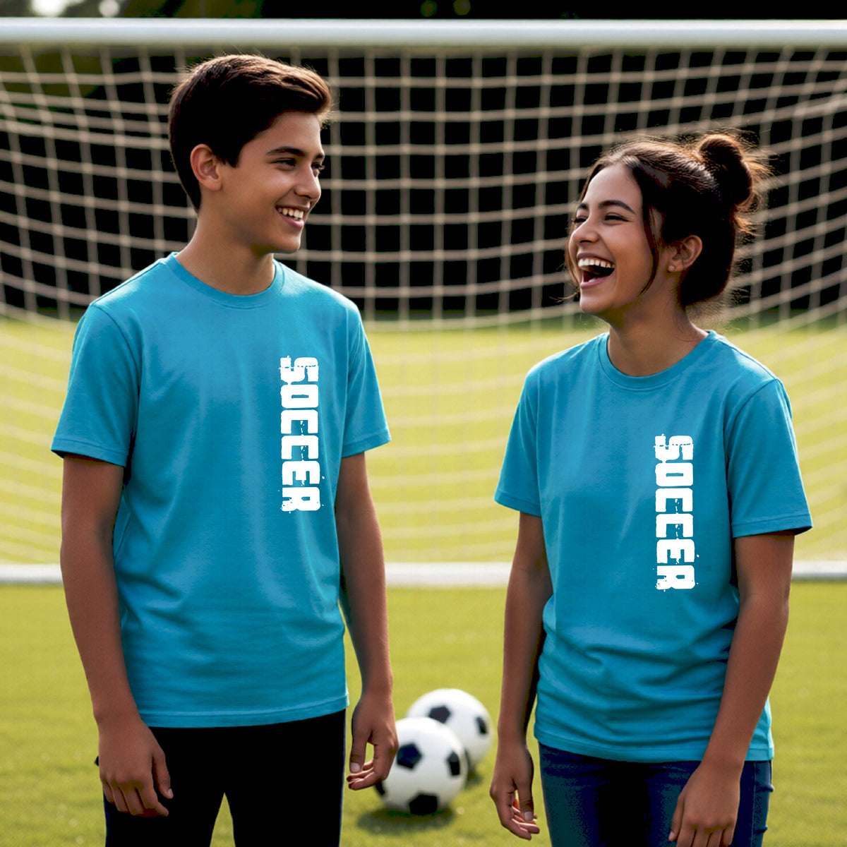 Two young students on a soccer field holding a soccer ball, wearing a bright blue t-shirt with a white graphic of the word 'SOCCER' in block font printed down the side of the shirt