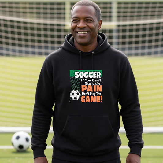 A smiling man on a soccer field while wearing a black hoodie pullover with the graphic slogan 'SOCCER If You Can't Stand the PAIN Don't Play The GAME!' in green, white, and orange text.