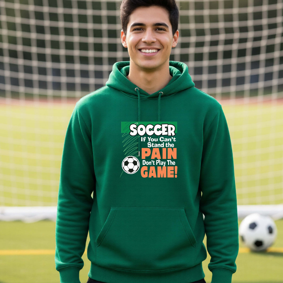 A smiling man on a soccer field while wearing a green hoodie pullover with the graphic slogan 'SOCCER If You Can't Stand the PAIN Don't Play The GAME!' in green, white, and orange text.