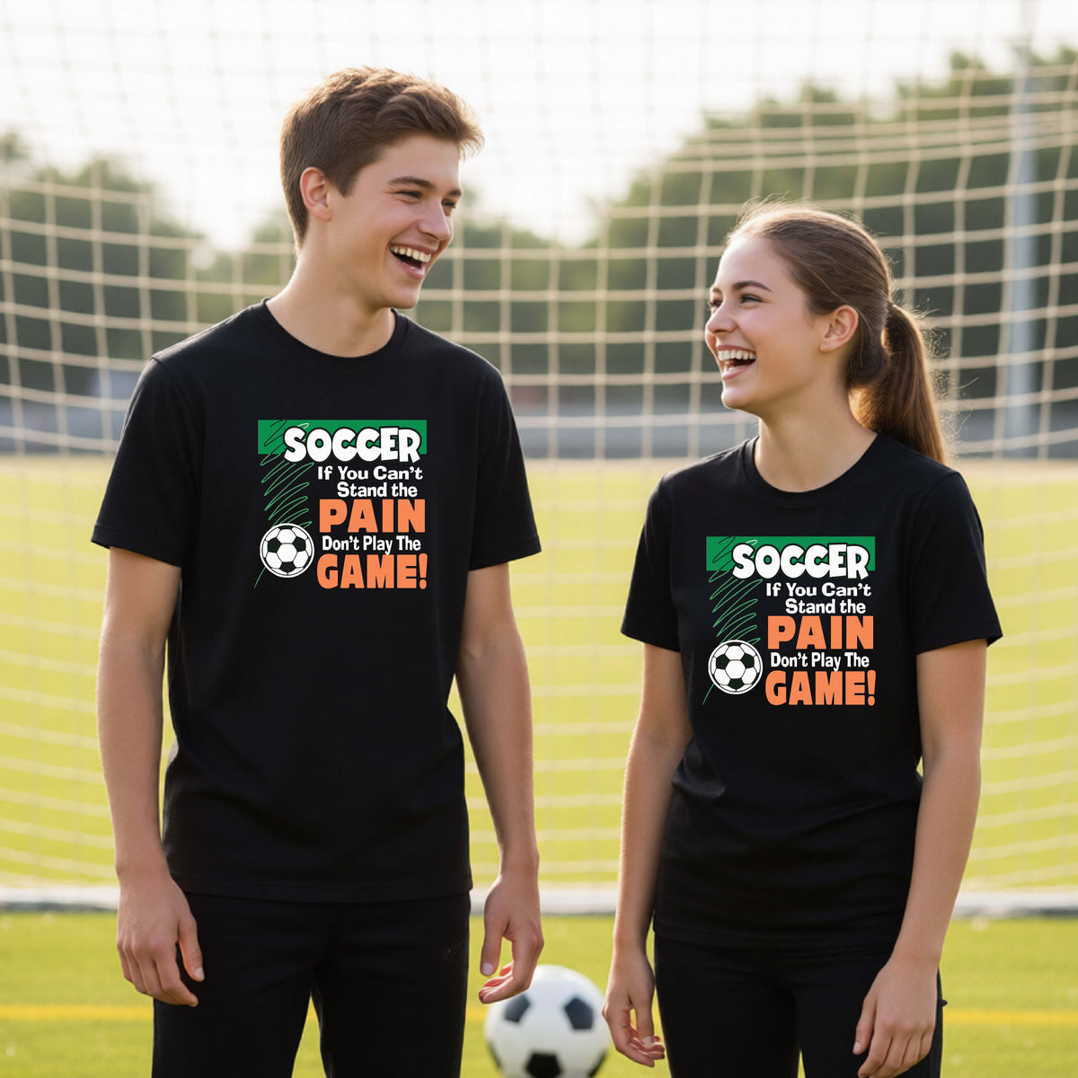 Two young people standing on a soccer field wearing matching black t-shirts with a colorful graphic that reads 'SOCCER If You Can't Stand the PAIN Don't Play the GAME!' in green, white, and orange. A soccer ball is on the grass in front of them, with a soccer net and trees in the background.