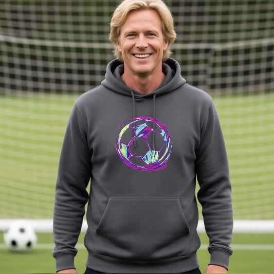 A smiling man wearing a dark gray hoodie with a colorful irridescent soccer ball graphic on the chest, standing on a soccer field with a goal net in the background.