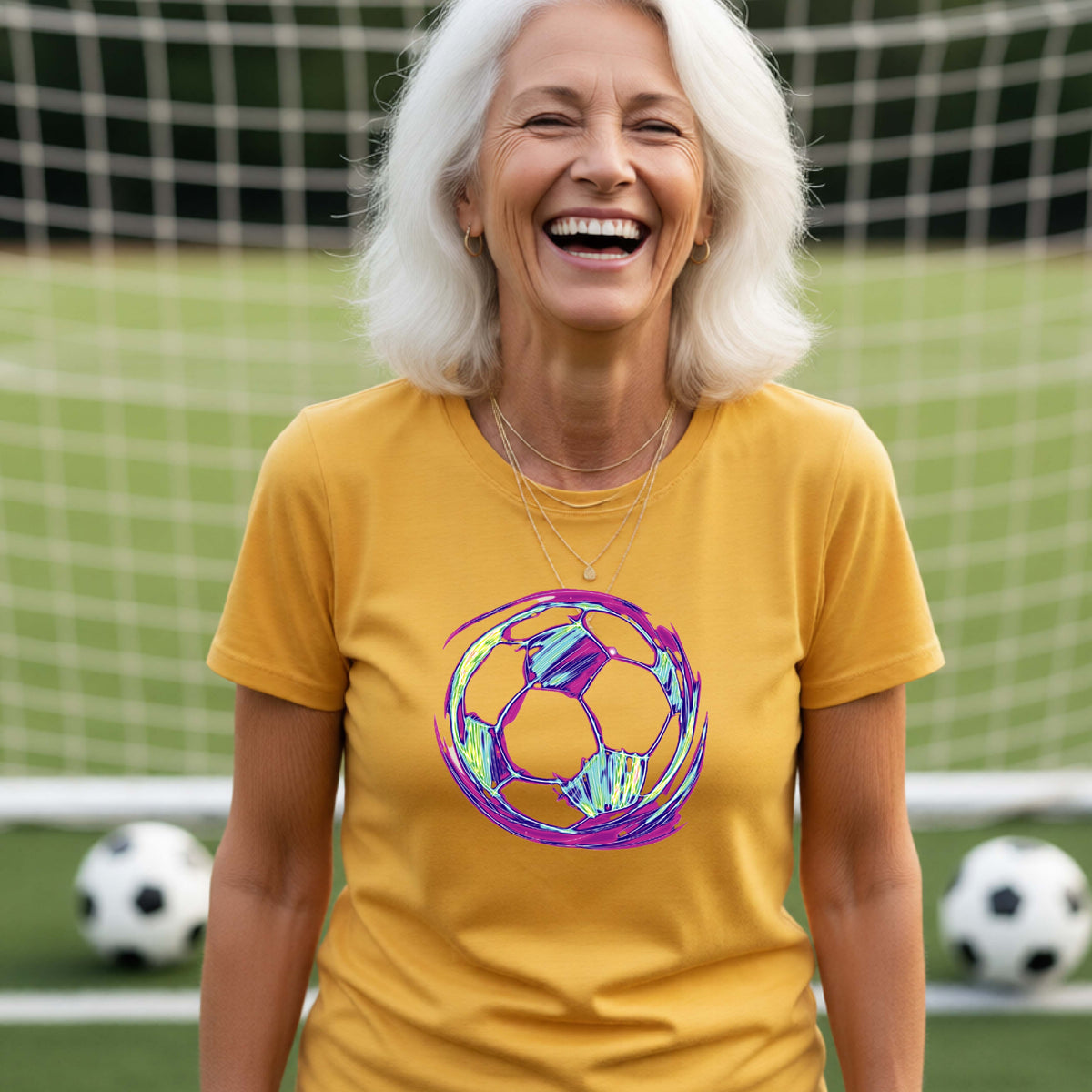 A woman smiling on a soccer field wearing a gold t-shirt with a colorful, iridescent soccer ball graphic on the chest.