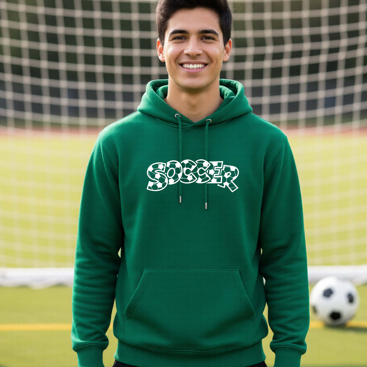 A smiling man wearing a green hoodie pullover , standing on a soccer field in front of a goal net. with a white graphic of the word 'SOCCER' in a stylish soccer pattern printed on the chest.