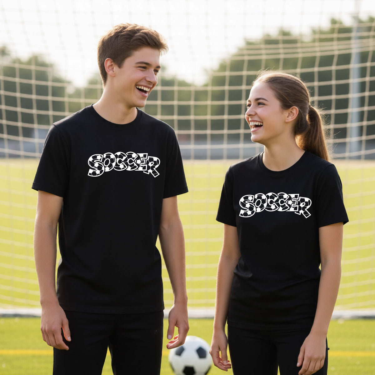 Two young athletics wearing matching black t-shirt, standing on a soccer field in front of a goal net. with a white graphic of the word 'SOCCER' in a stylish soccer pattern printed on the chests.